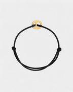 Pulsera de cordón negro con un broche dorado sobre un fondo gris claro