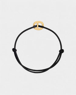 Black cord bracelet with a golden clasp on a light gray background