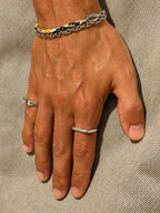 A close-up of a person's hand wearing multiple silver rings, including a thin band ring on the ring finger, with a beaded bracelet on the wrist, set against a textured beige fabric background.