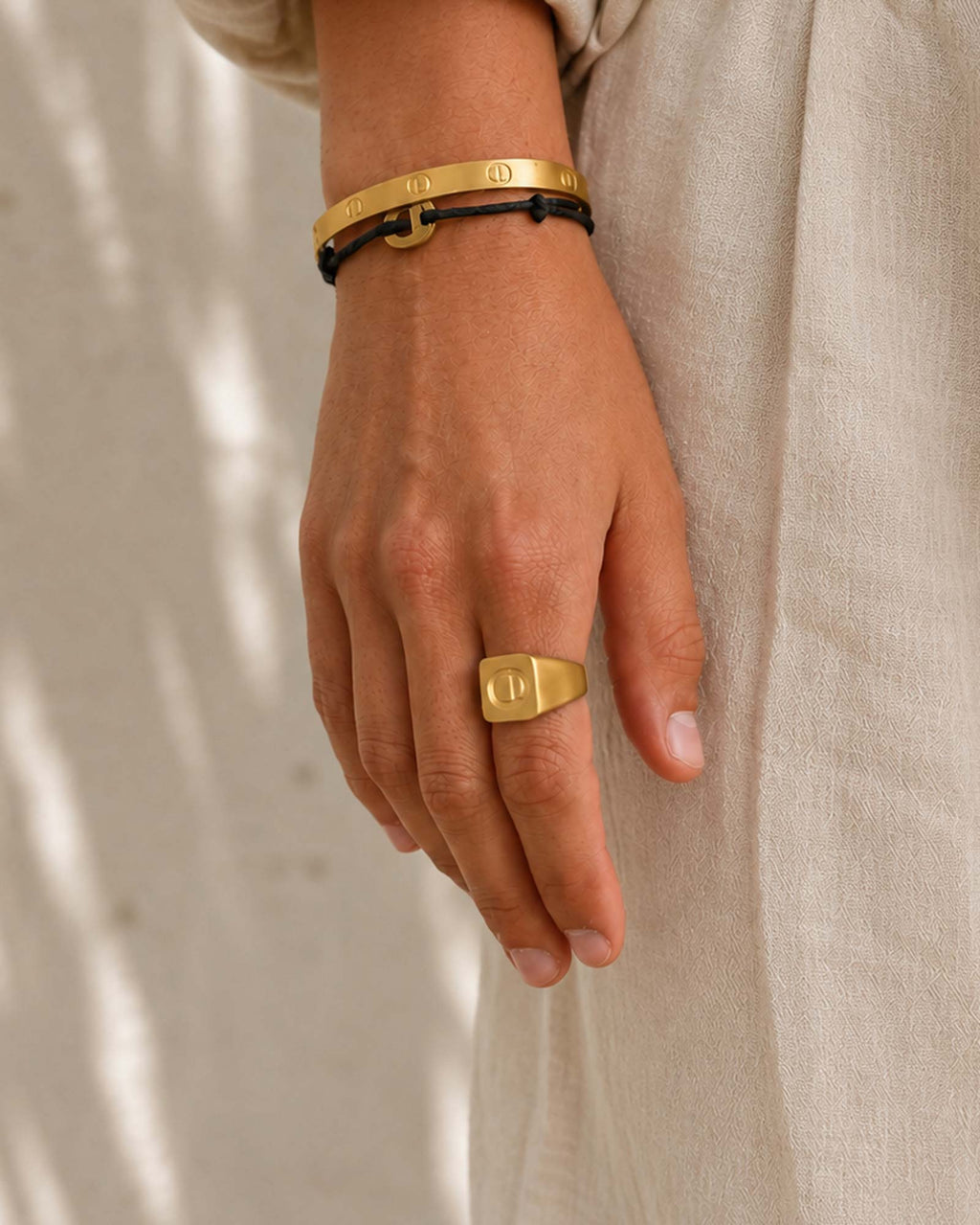 Hand wearing a gold ring and bracelet on a neutral background