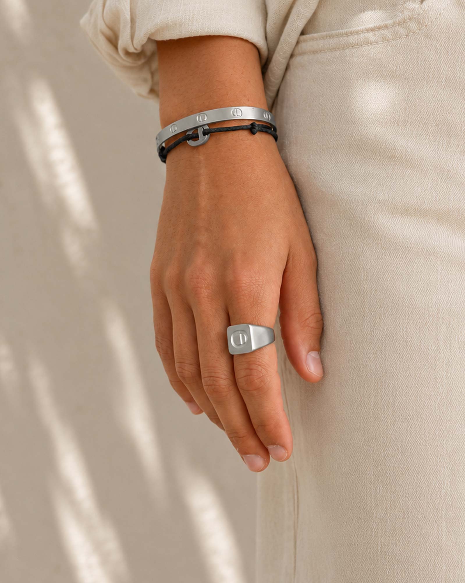 Hand wearing a silver ring and bracelets on a neutral background