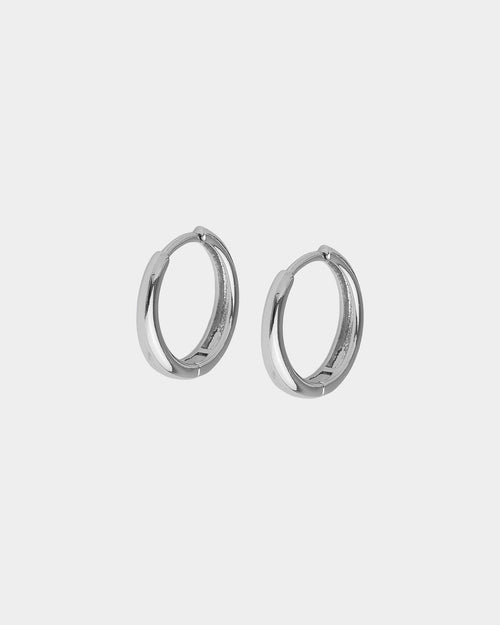 A pair of polished silver-tone huggie hoop earrings on a light gray background.