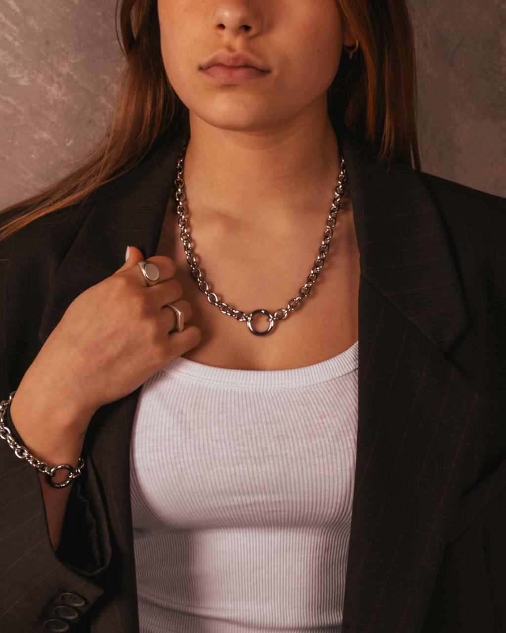 Person wearing a chain necklace and black blazer with a neutral background