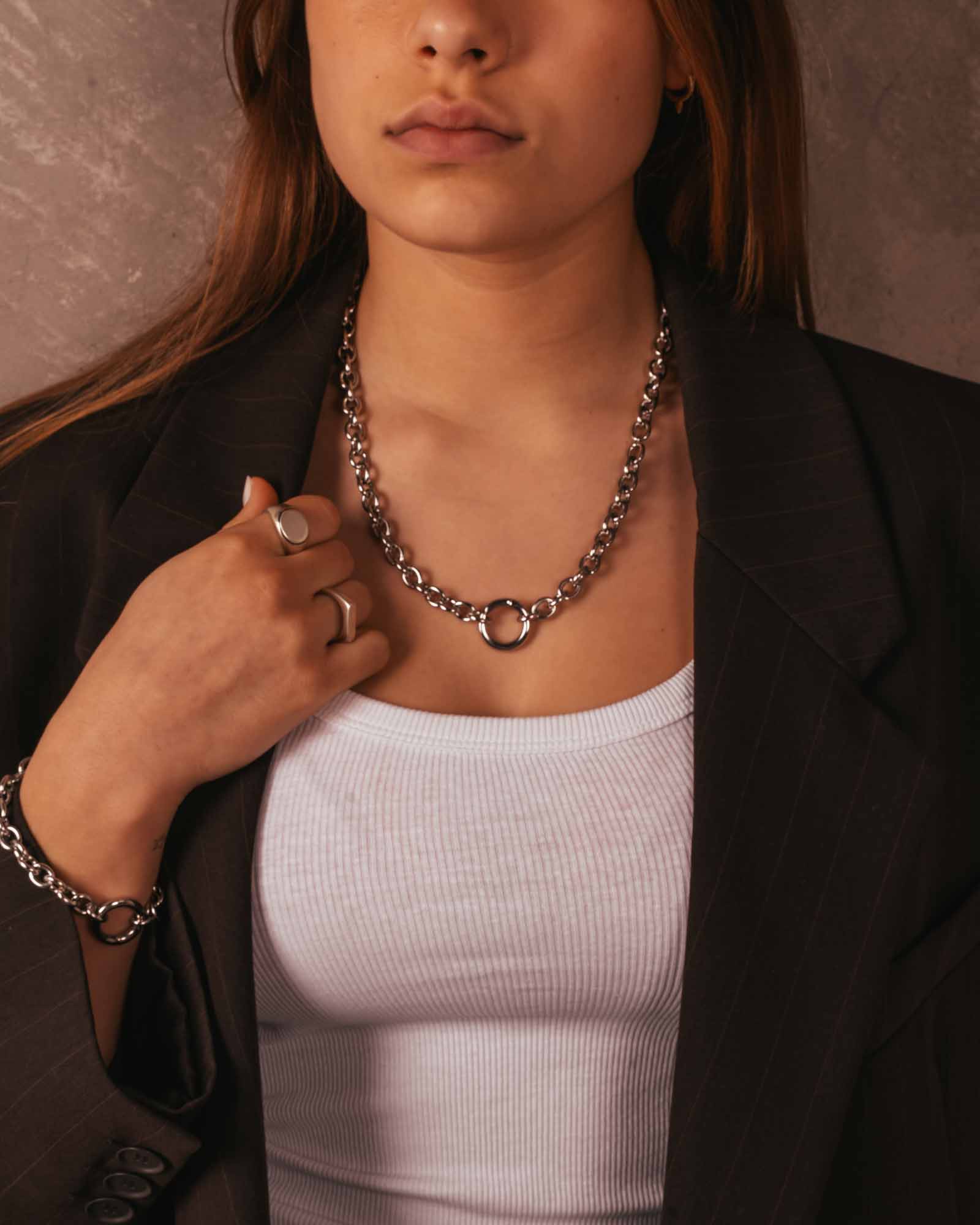 Person wearing a chain necklace and black blazer with a neutral background