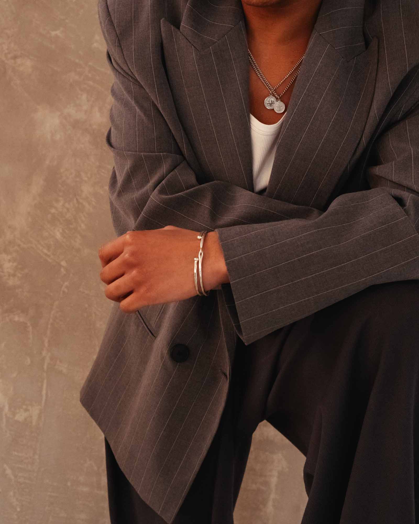 Person wearing a brown pinstripe suit with a neutral background and hook bracelet