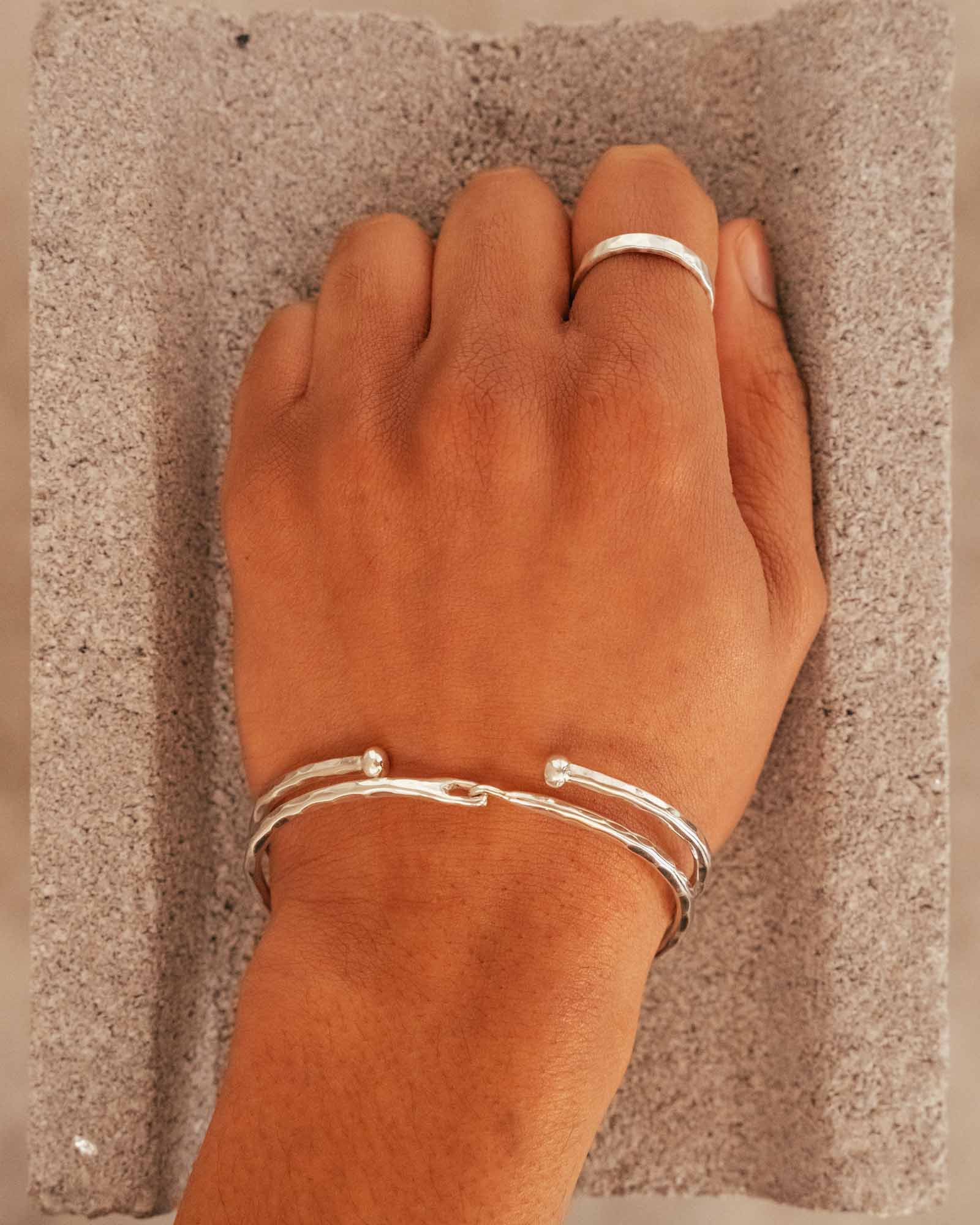 Hand wearing a silver ring and bracelet on a textured surface