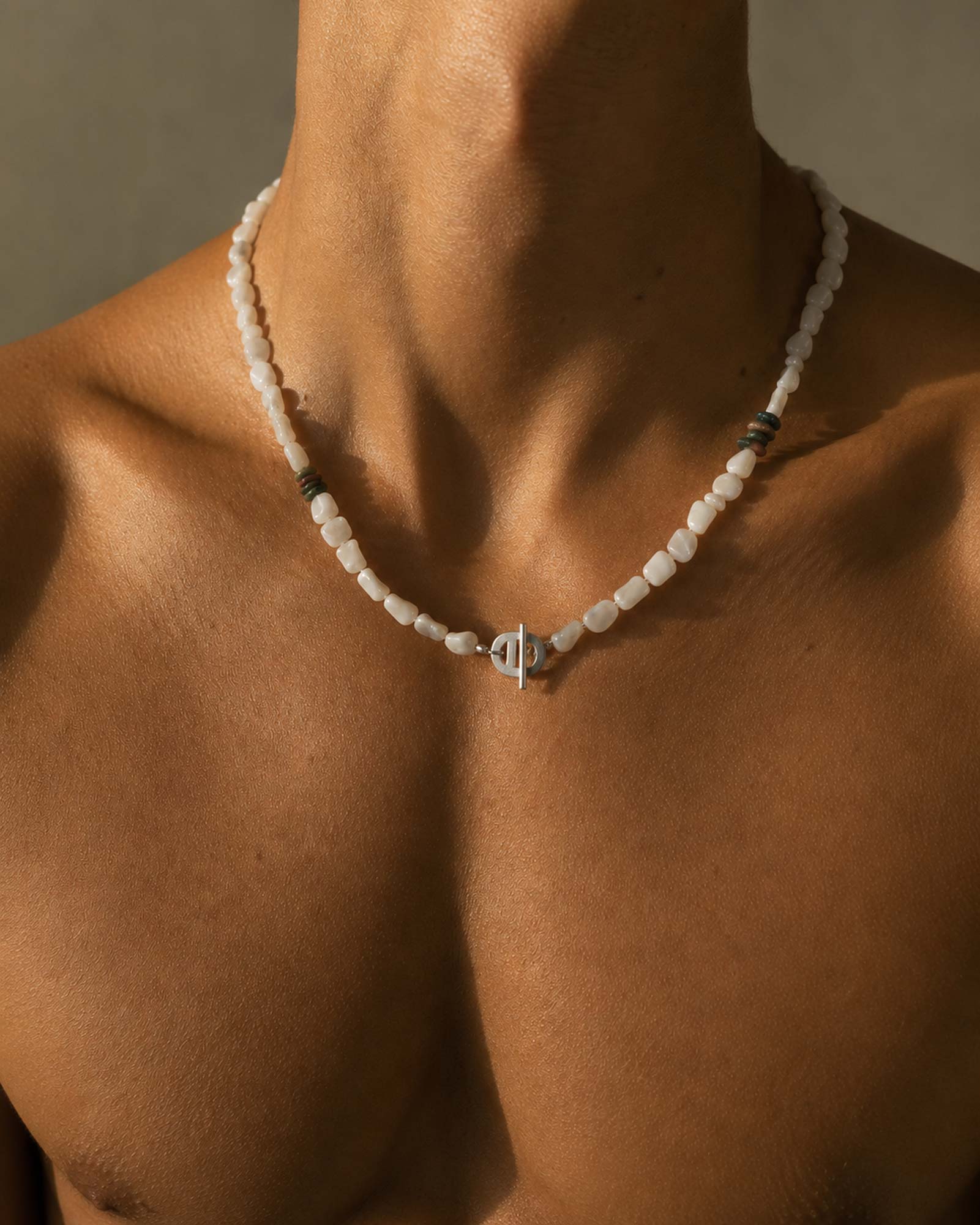 Necklace with a unique clasp on a person's neck against a neutral background