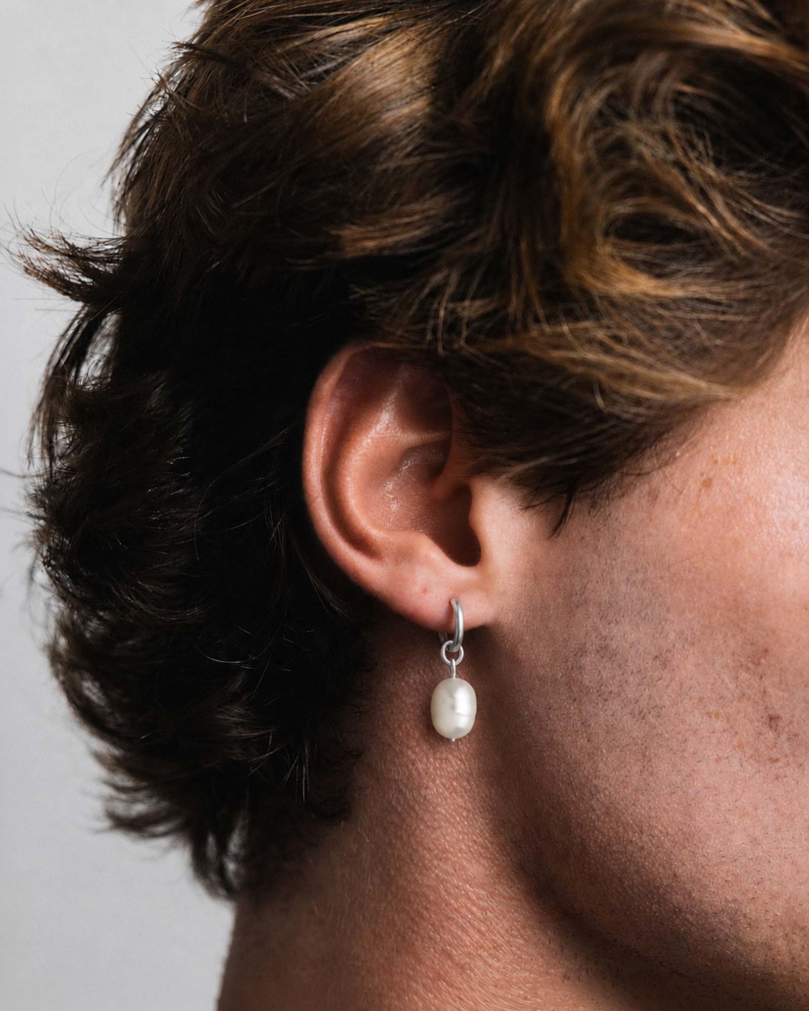 Close-up of an ear wearing a pearl earring with a neutral background