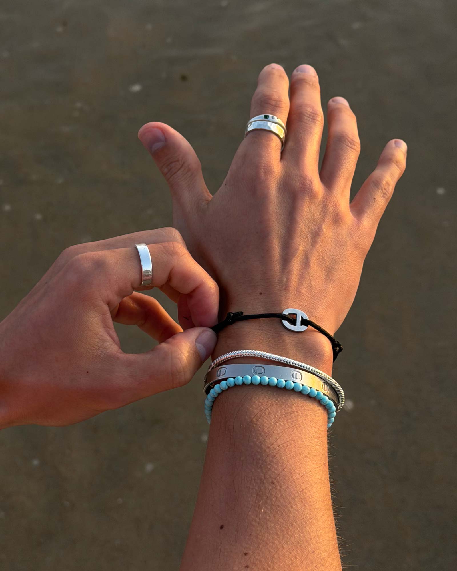 Close-up of a person's hands with multiple bracelets on a sandy background