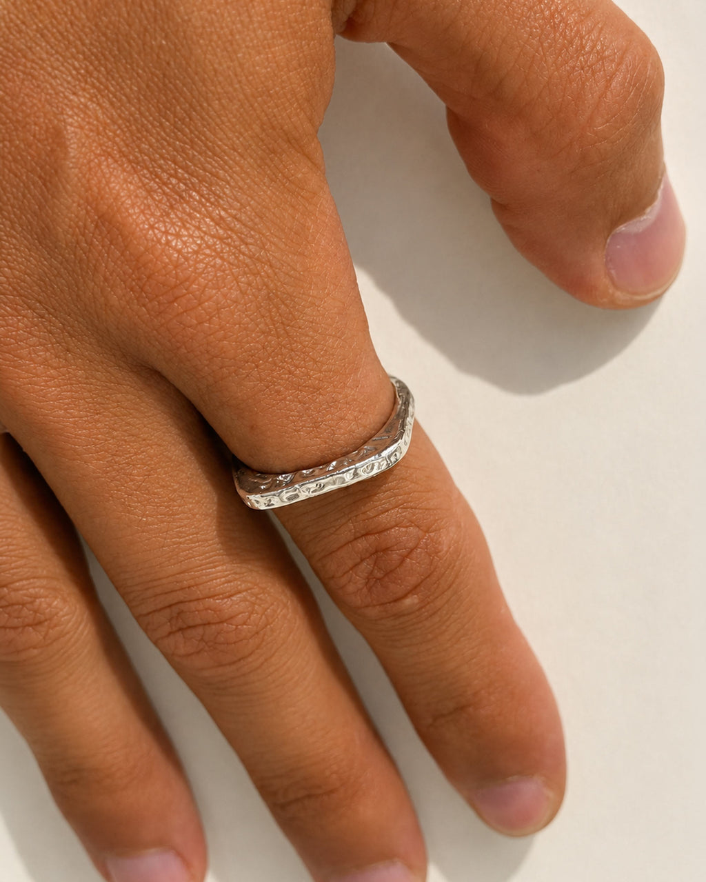 A close-up of a hand wearing a slim silver band ring with a row of small clear stones, photographed against a plain light background.