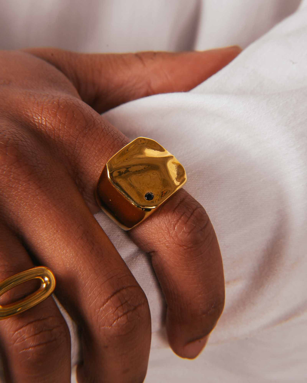 Gold ring with a blue gemstone on a hand against a white fabric background