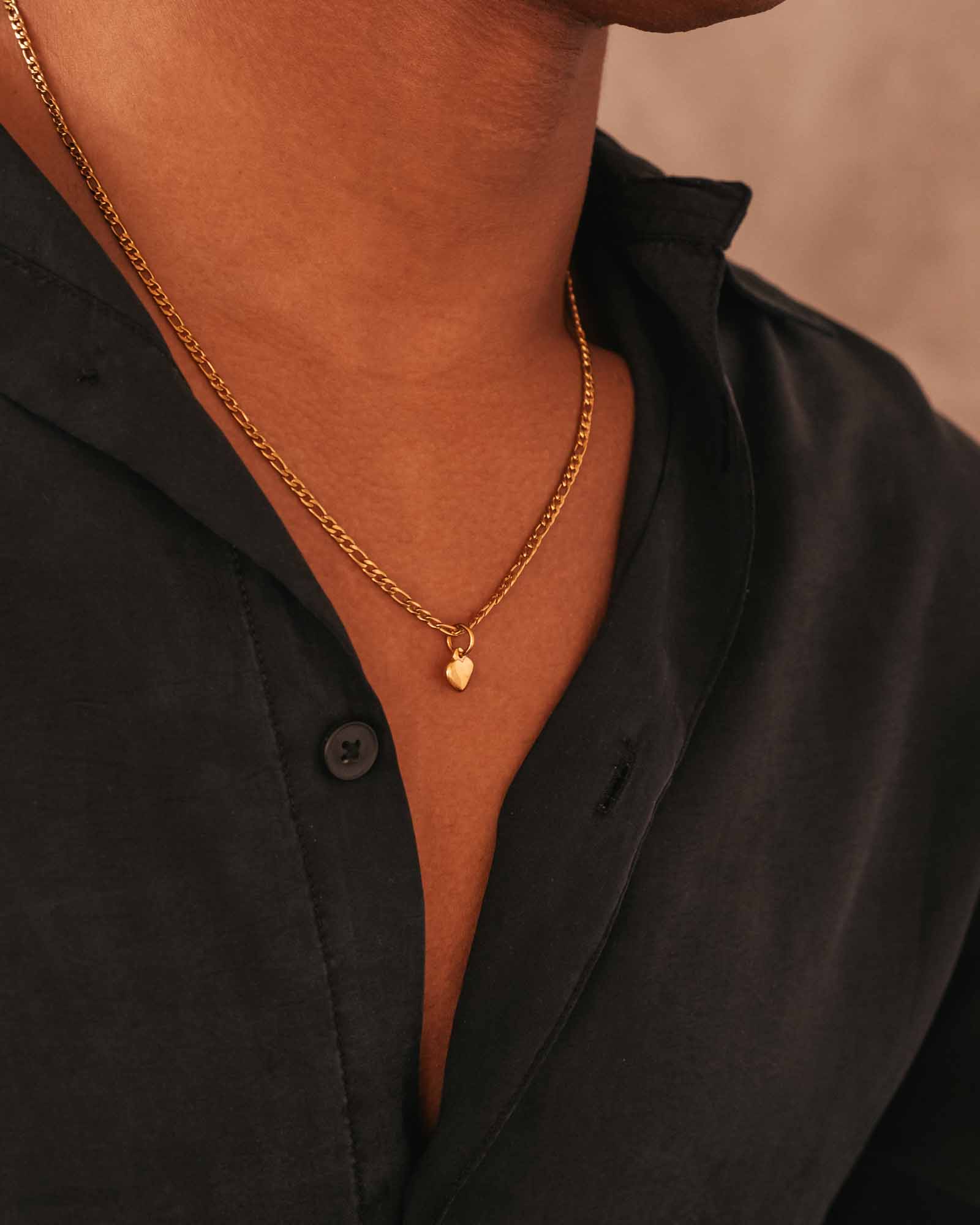 Person wearing a gold necklace with a heart pendant against a neutral background