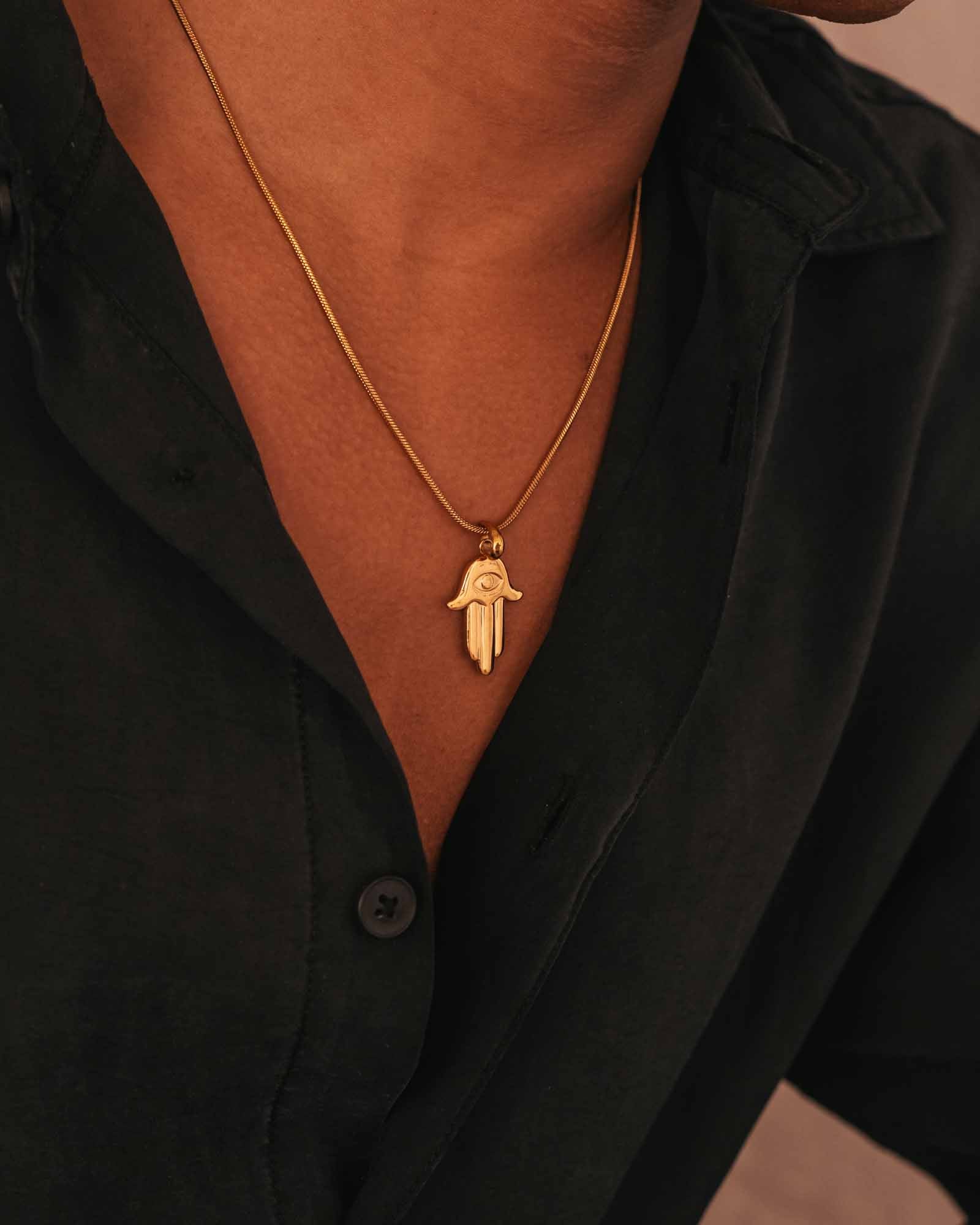 Gold necklace with a hamsa pendant worn by a person in a black shirt.