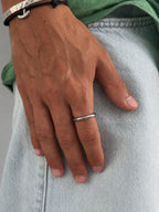 Un primo piano della mano di una persona appoggiata su jeans in denim chiaro, con un semplice e sottile anello a fascia d’argento all’anulare.