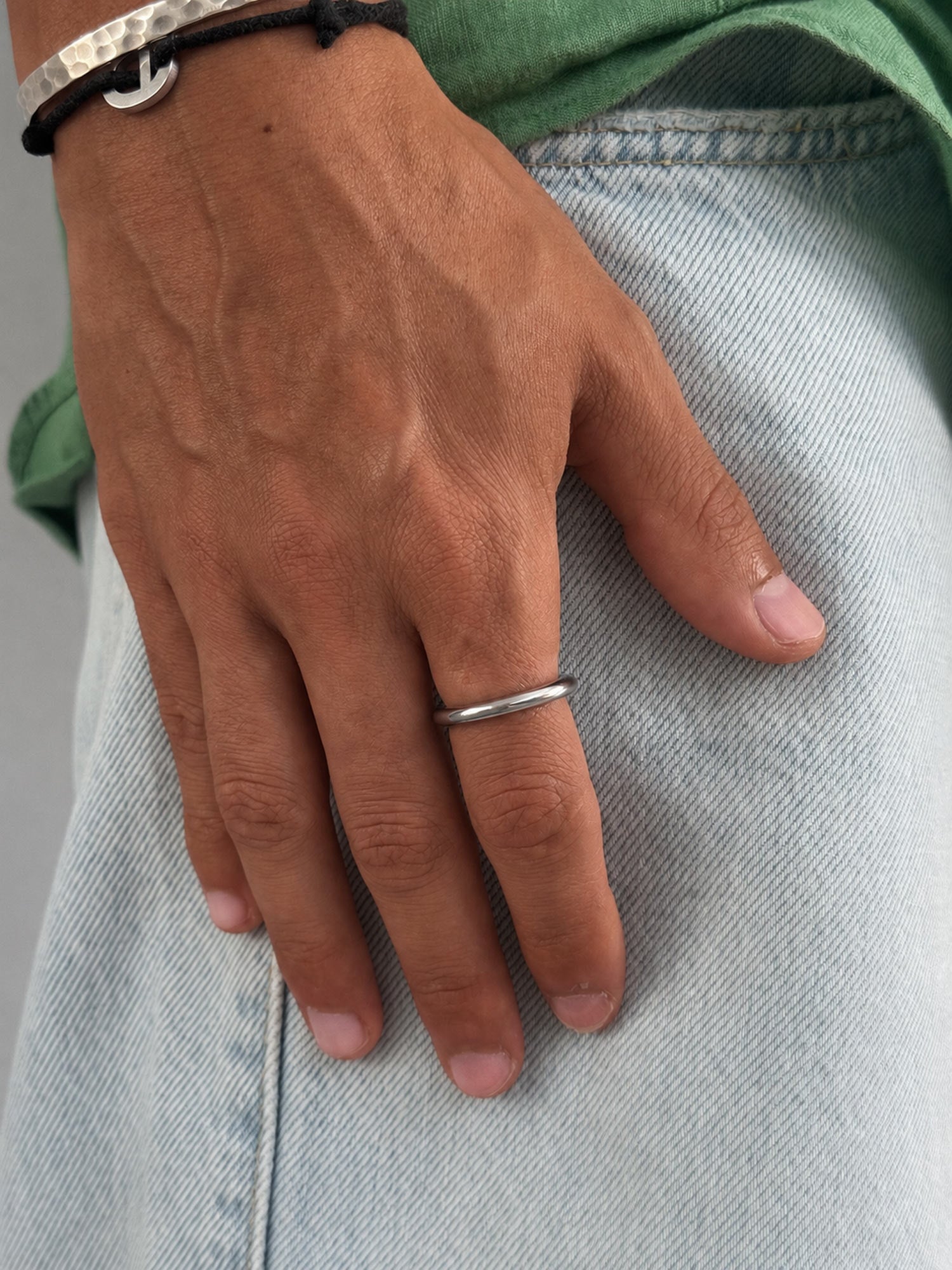 A close-up of a person's hand resting on light-wash denim jeans, wearing a simple, thin silver band ring on the ring finger.