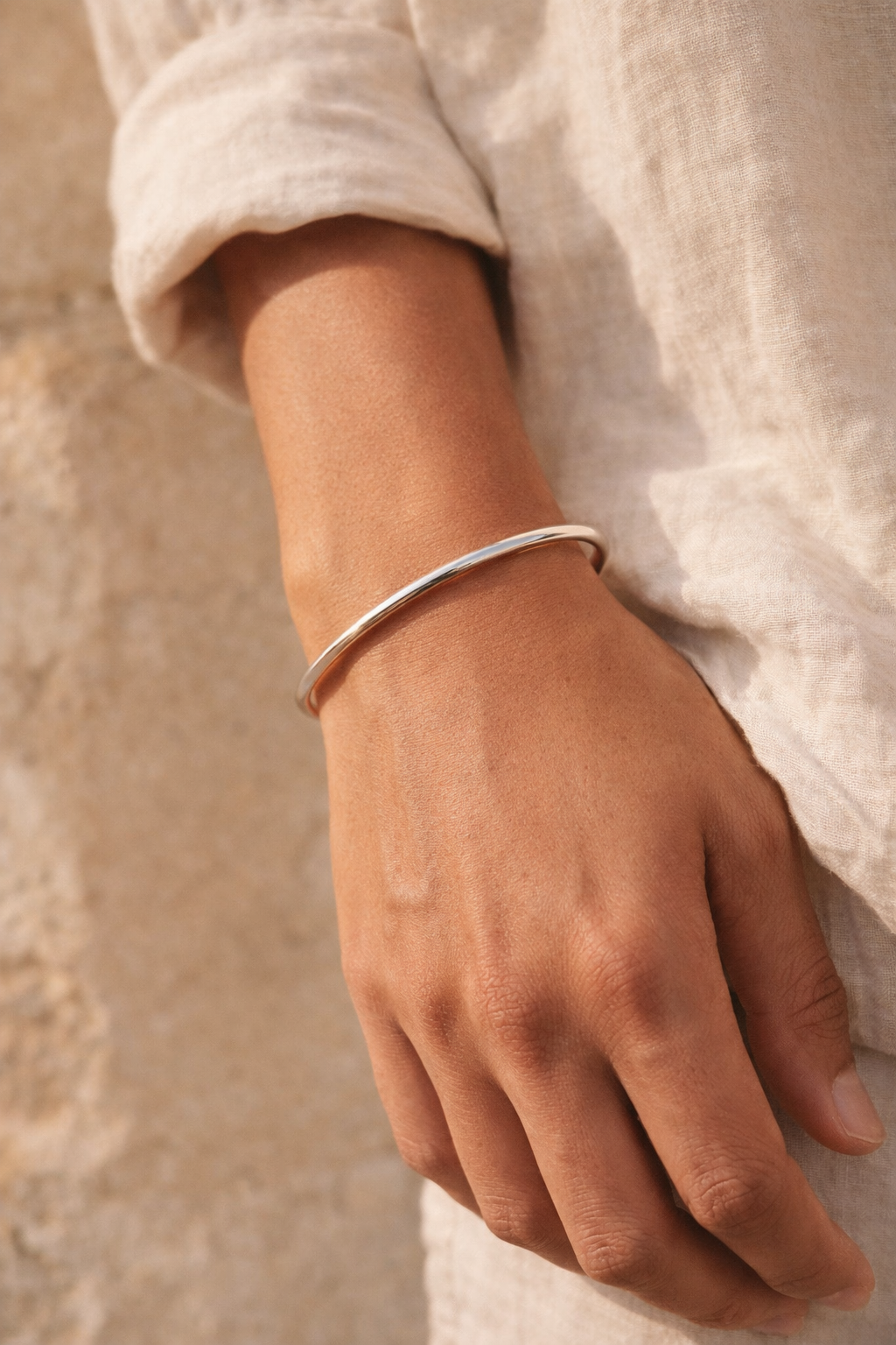 Hand wearing a silver bracelet against a neutral background