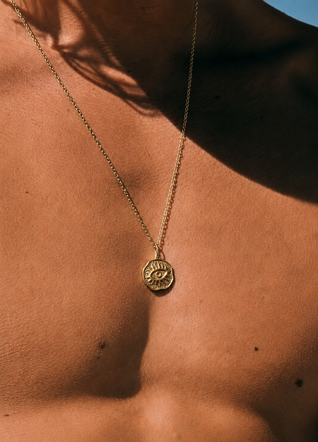 Gold necklace with a pendant on a person's chest against a blue sky.