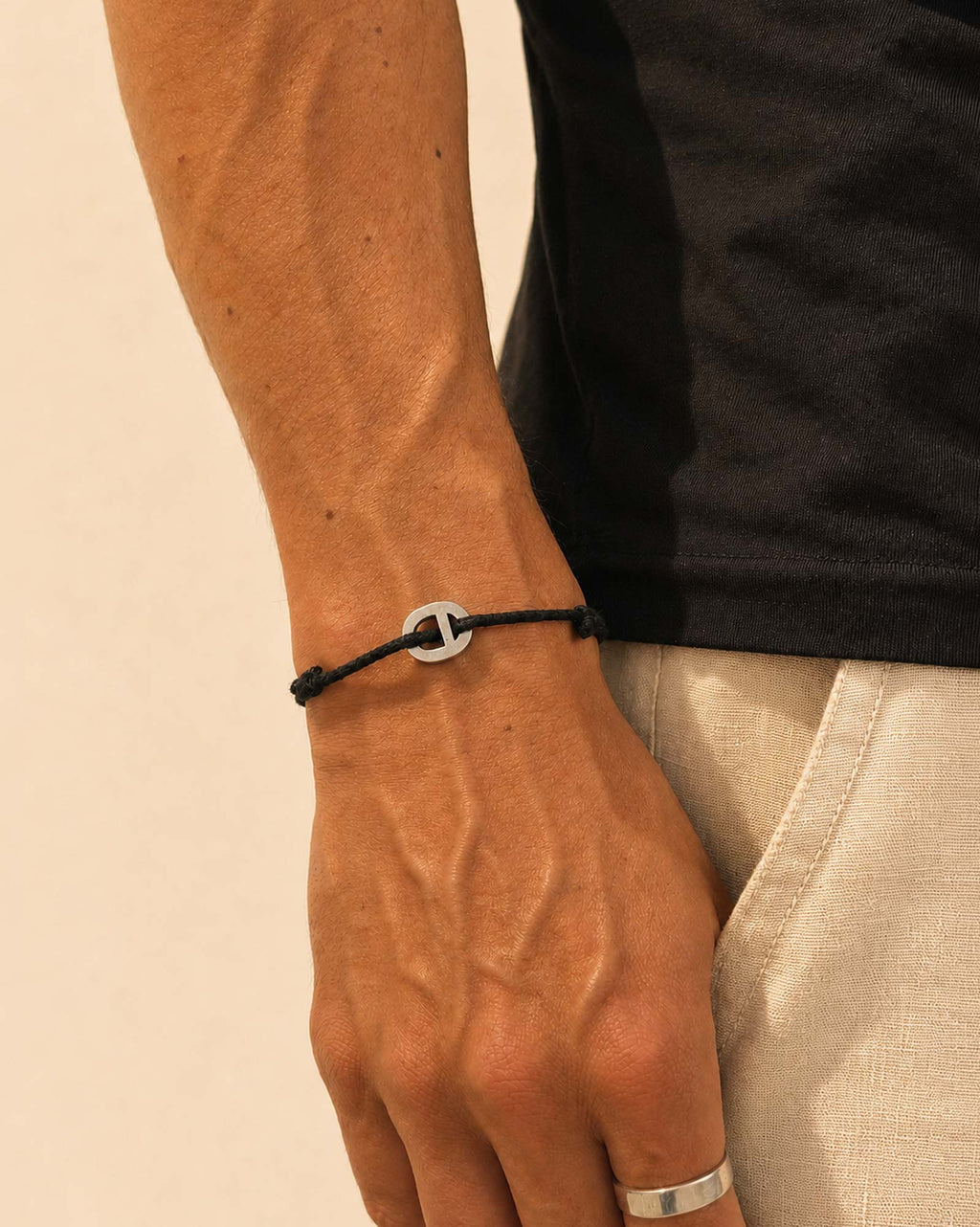 Close-up of a wrist wearing a black bracelet with a silver clasp on a beige background