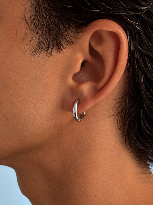 A close-up of a person's ear wearing a polished silver hoop earring.