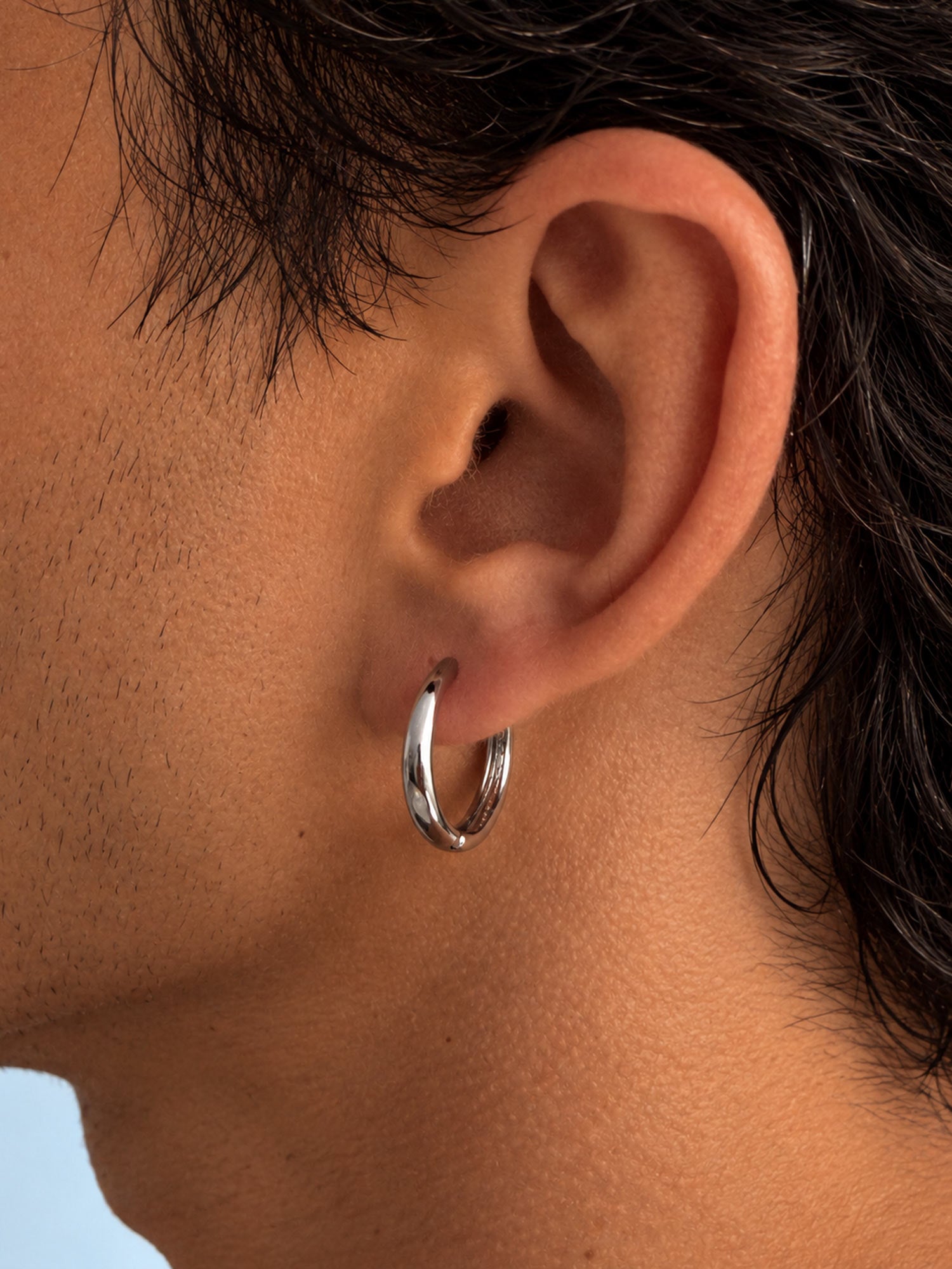 A close-up of a person's ear wearing a polished silver hoop earring.