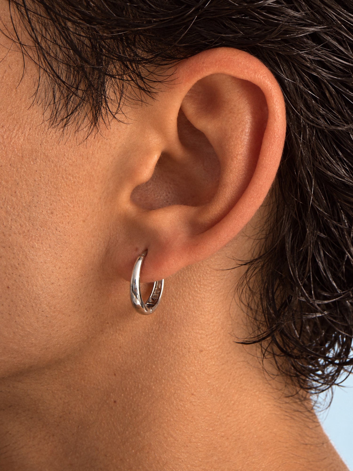 A close-up side profile of a person's ear wearing a polished silver hoop earring.