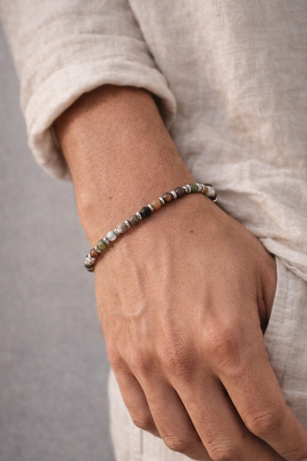 Close-up of a hand wearing a beaded bracelet on a neutral background - Milos Bracelet