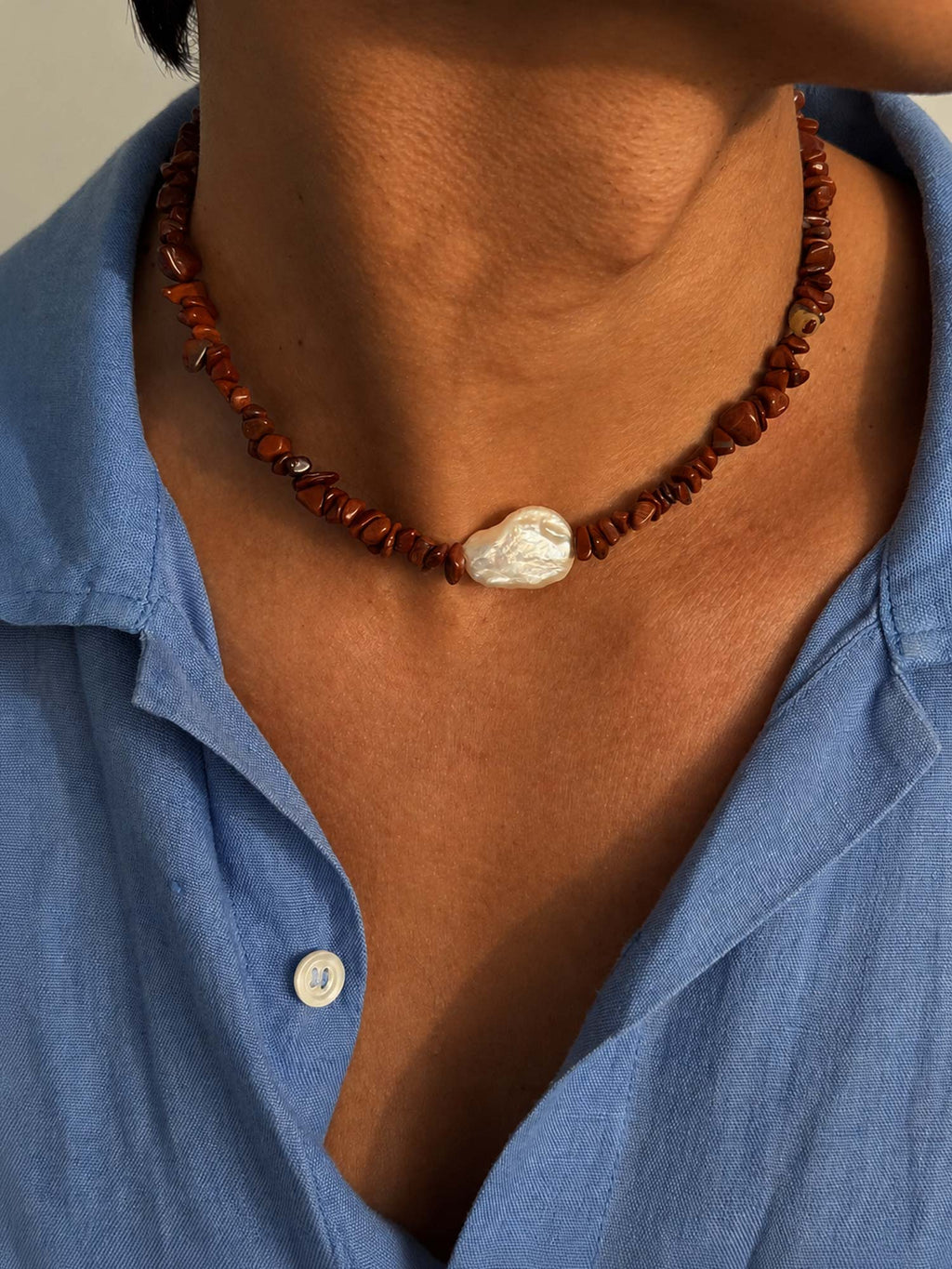 Necklace with a large central bead worn by a person wearing a blue shirt.