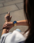 Reloj cronómetro - Bisel azul con correa dorada en la muñeca de la modelo - Relojes Online - Dicci